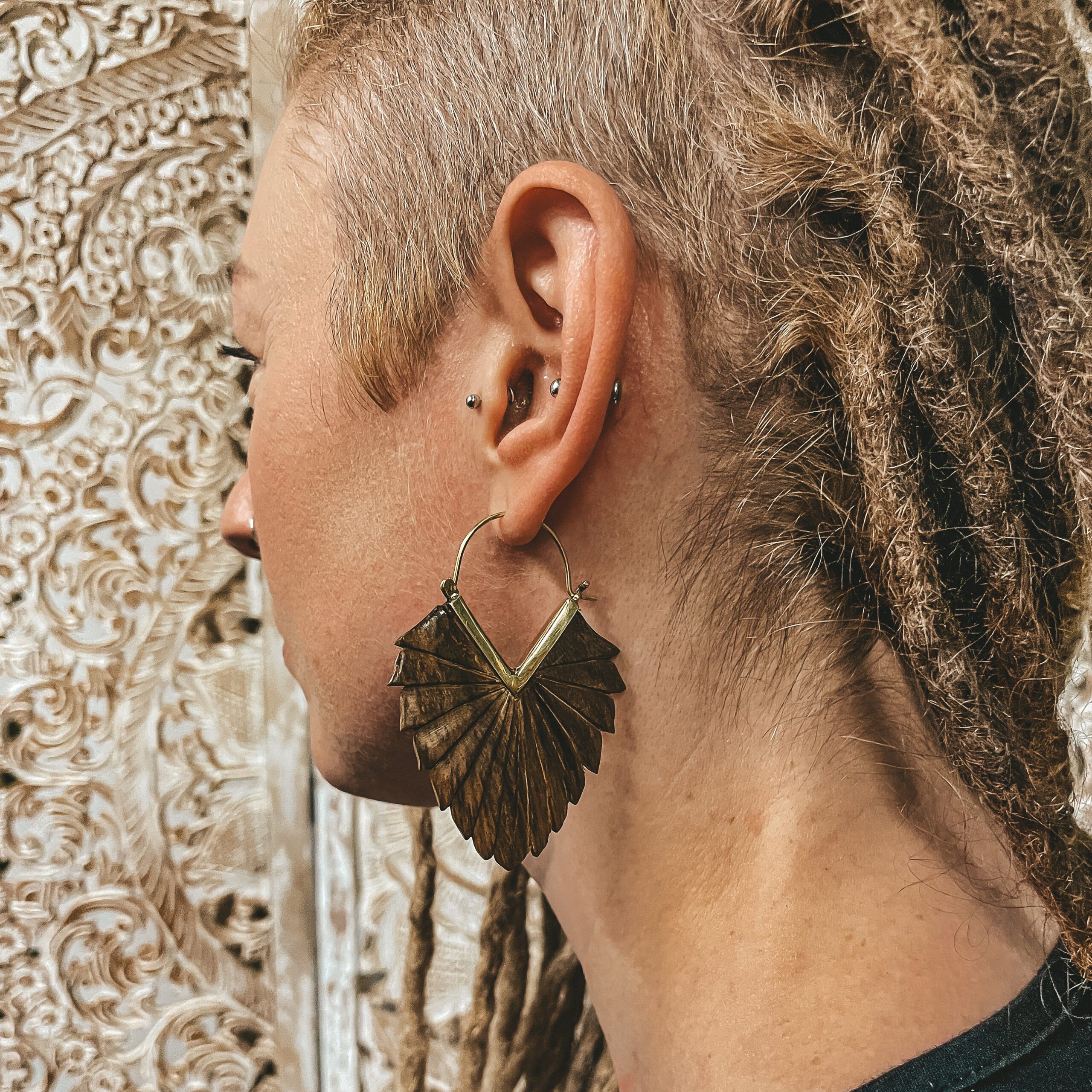 Wooden Sago Tribal Earrings Handmade Ethnic Carved Wood with a Bronze Clasp in gold colour on a blonde girl with dreadlocks and engrabed wooden distressed white backdrop boho style