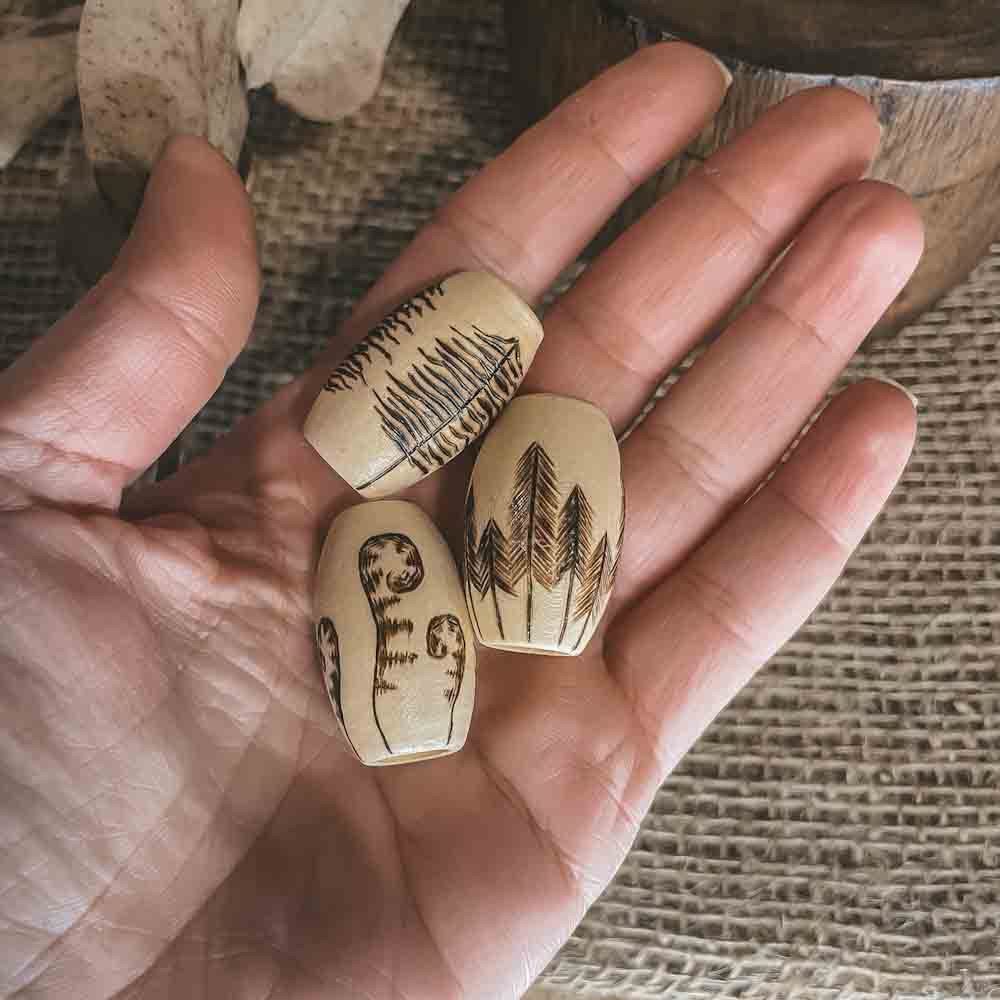 hand burned forest designs on large wooden dreadlock beads held in a hand